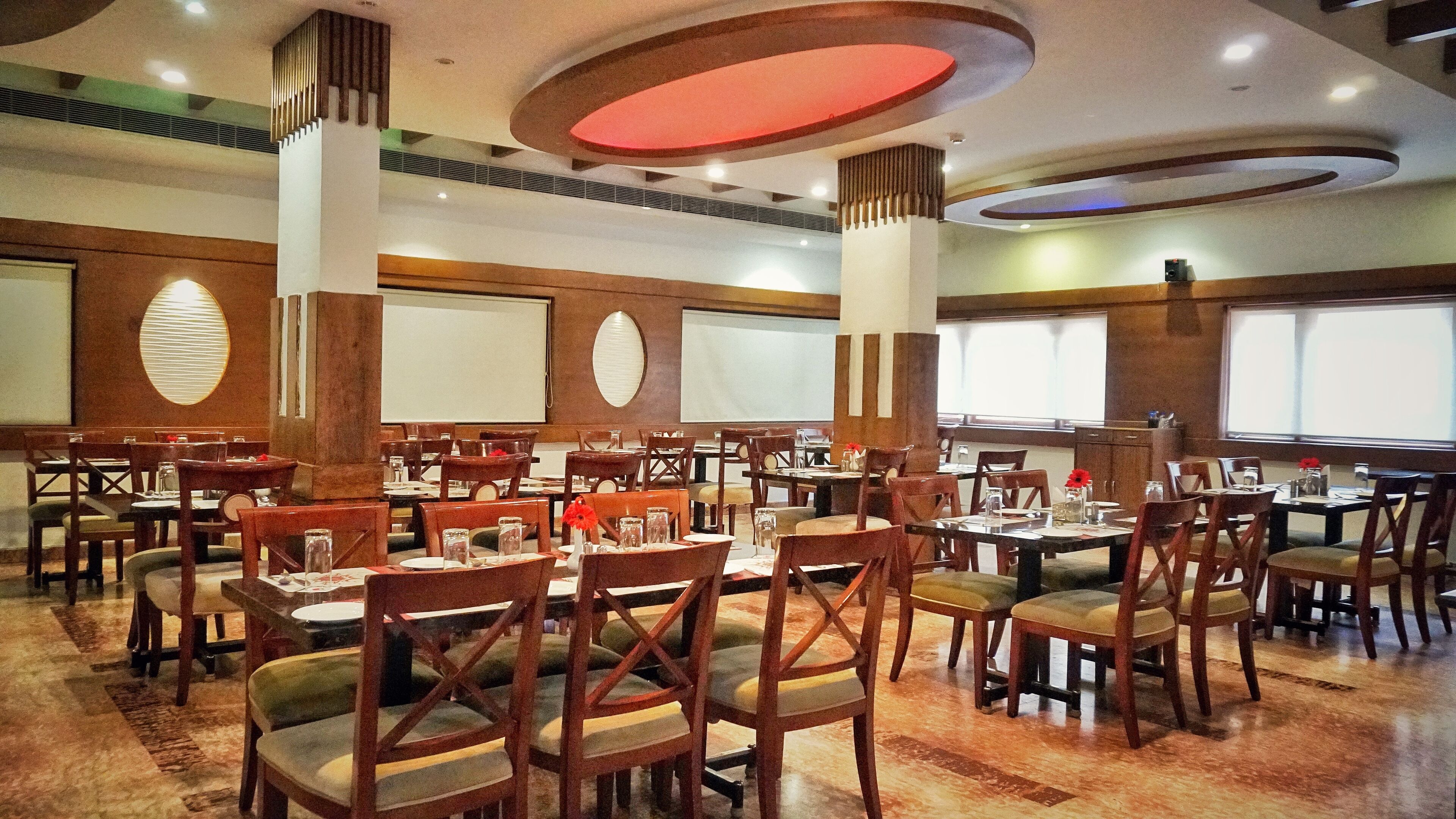 A spacious dining area with multiple tables and chairs, large windows, and a modern ceiling design.