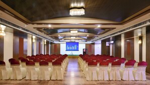 A conference room with rows of chairs, a large screen at the front, and a chandelier.