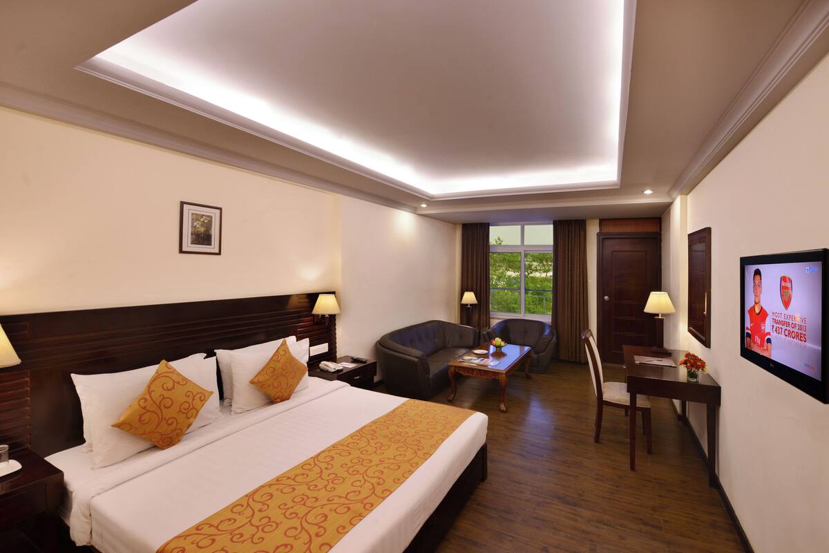 A hotel room with a large bed, two bedside tables, a desk with a chair, a TV, and a window with curtains.