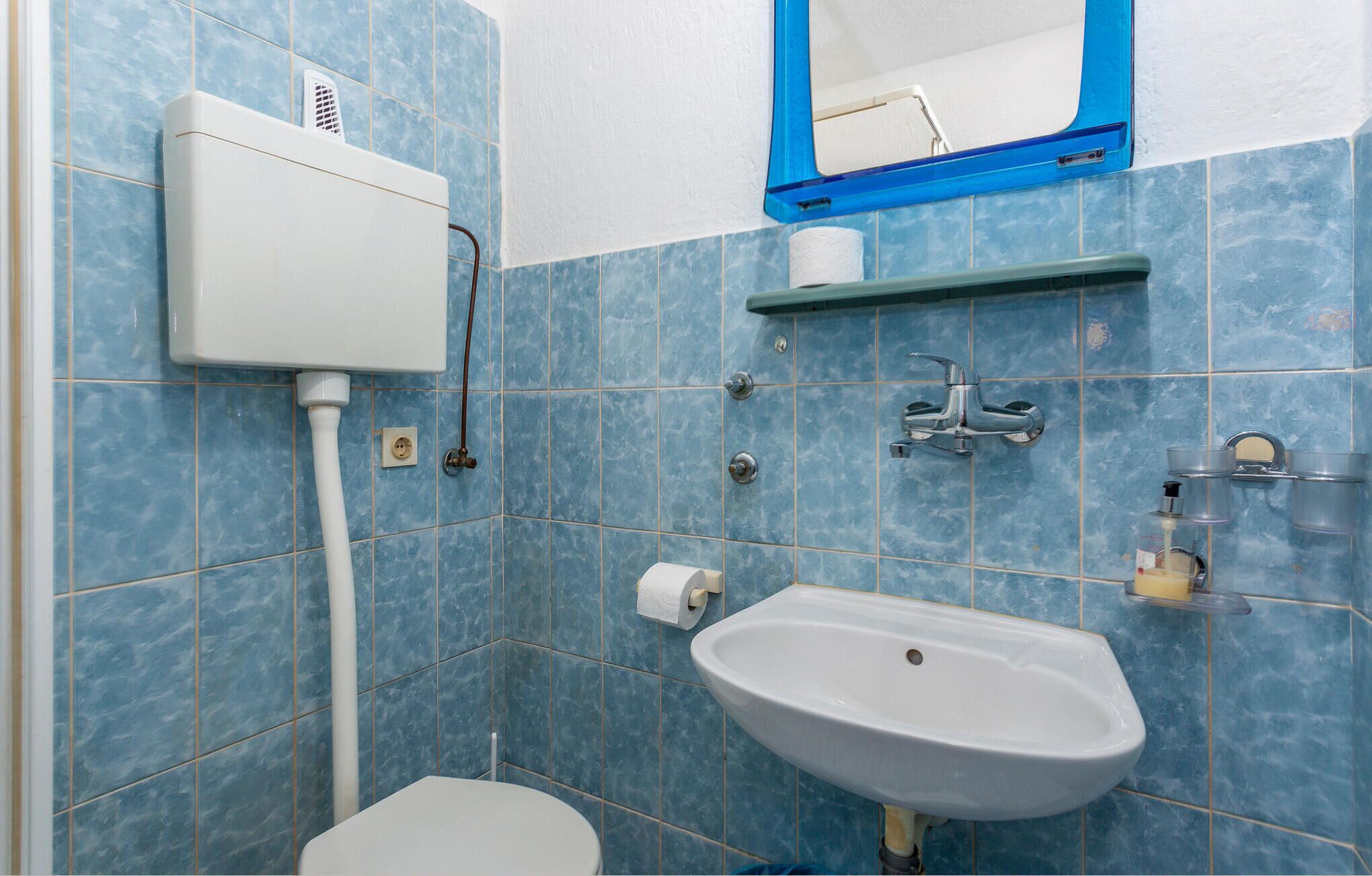 Ein Badezimmer mit Toilette, Waschbecken, Spiegel und blauen Fliesen.
