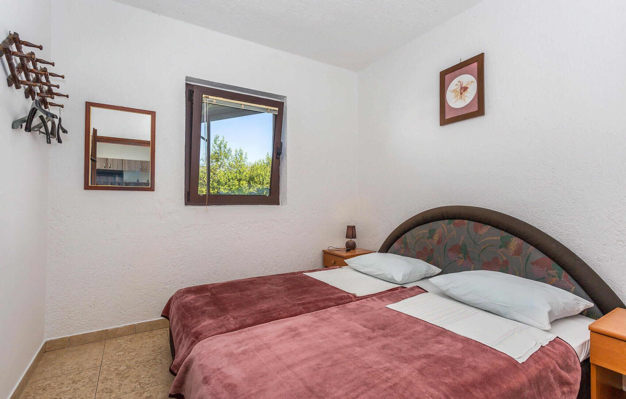 Une chambre à coucher avec un lit, une fenêtre, une table de chevet, une lampe et un tableau encadré au mur.