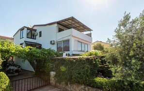 A modern two-story house with a flat roof, large windows, and a covered patio area.