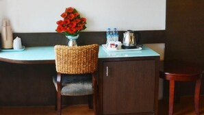 Una habitació petita amb un armari de fusta, una cadira de vimet, un ram de flors vermelles en un vas, una safata amb ampolles d'aigua i una tetera, i una pissarra a la paret.