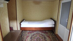 Una habitación pequeña con una cama individual, cabecera de madera, alfombra estampada y paredes color beige.