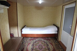 A small, single-bed room with a wooden headboard, a patterned carpet, and beige walls.