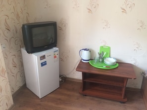 A compact refrigerator with a microwave on top, a green cutting board, a kettle, and a tray with plates and utensils.