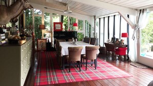 Un coin repas avec une table en bois, des chaises et un tapis à carreaux. On y trouve également une cheminée, un téléviseur et une fenêtre avec des rideaux.