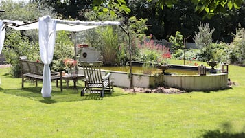 Een tuin met een houten bank, een tafel en een pergola met witte stof.