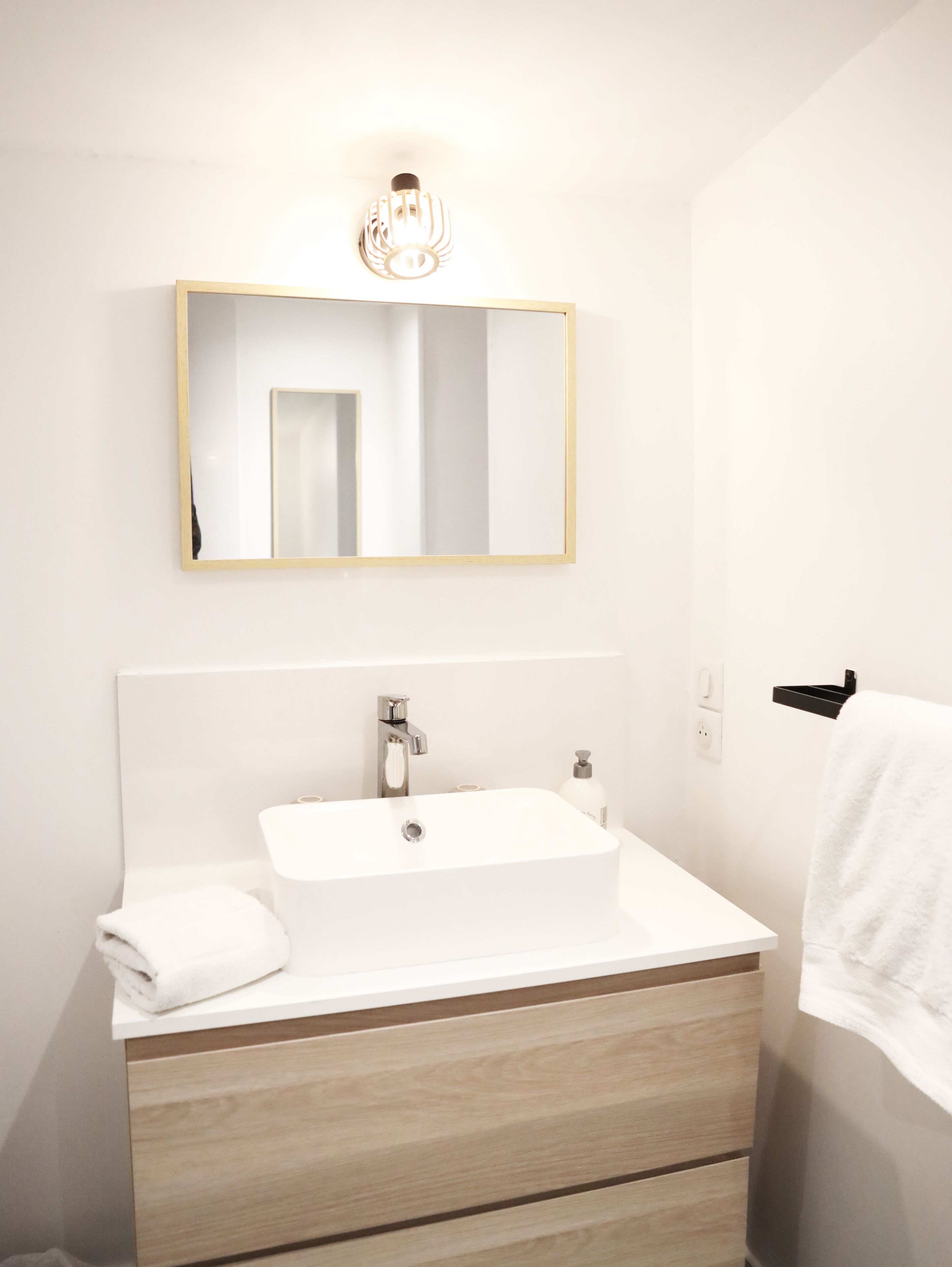 Une salle de bain moderne avec un lavabo blanc, un meuble-lavabo en bois et un miroir doté d’un cadre doré.