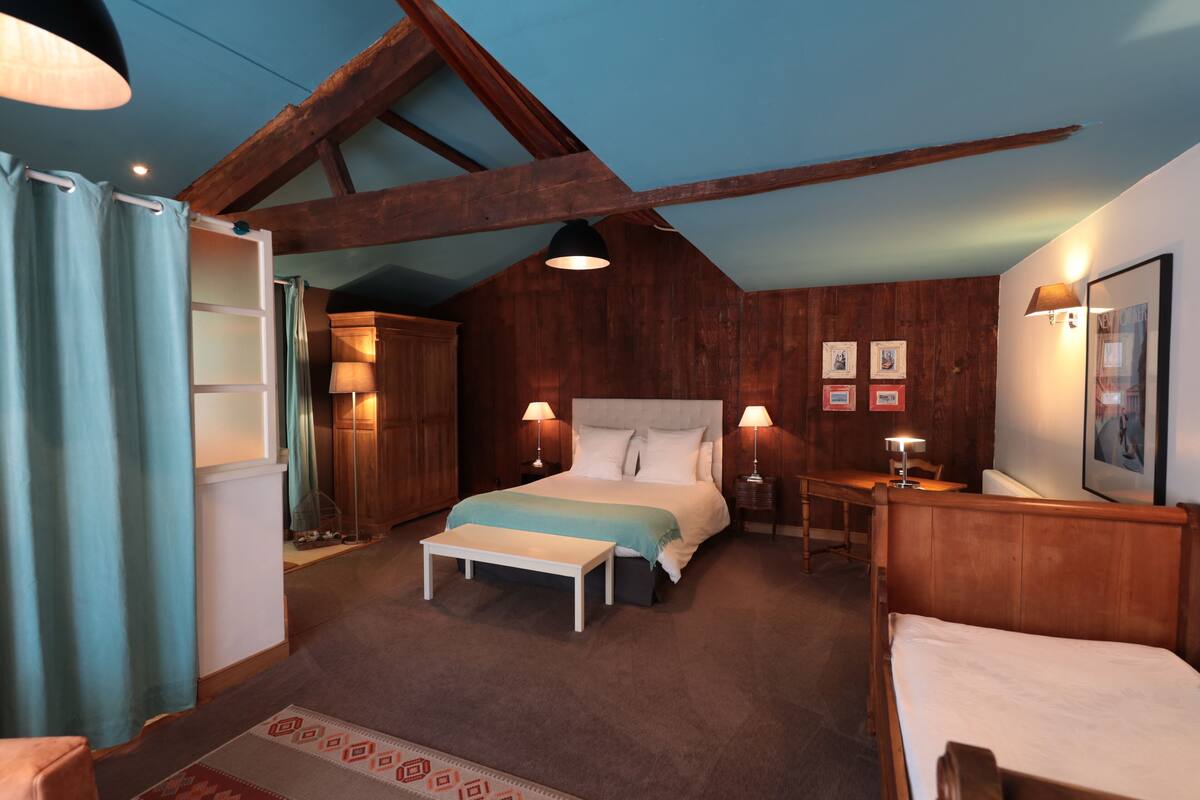 Une chambre avec un plafond en bois, un lit doté d’une tête de lit blanche, une table de chevet avec une lampe et un banc.