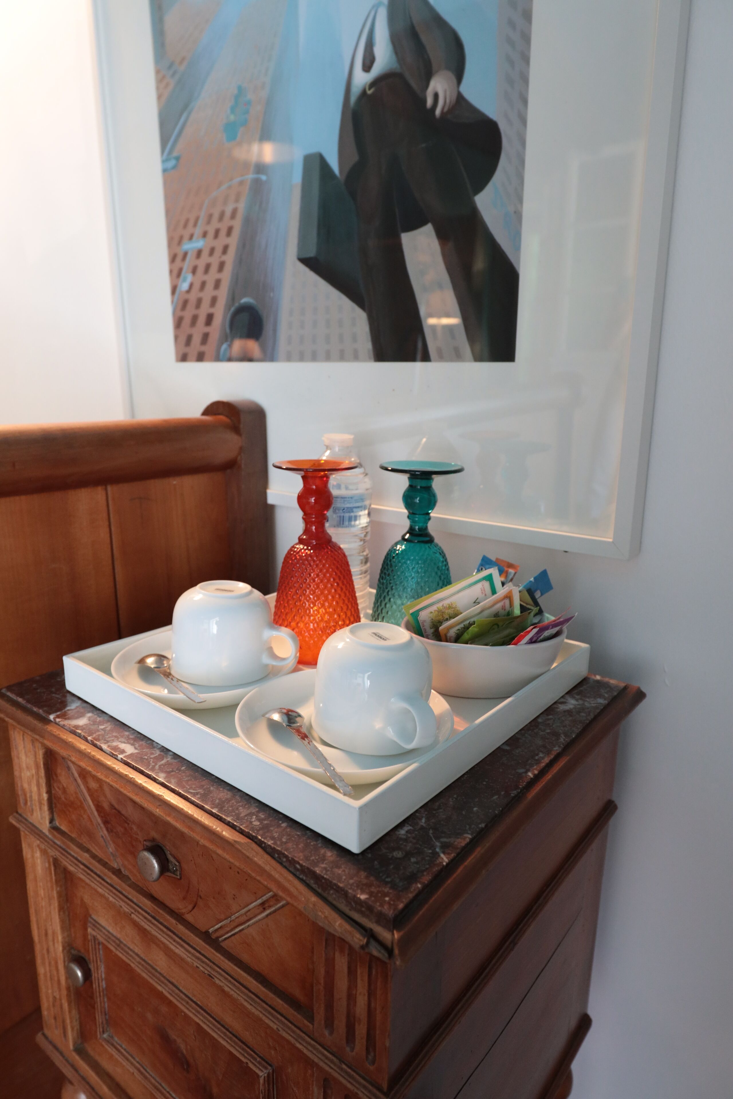 A wooden dresser with a tray holding white teacups, a red vase, and a teal vase with cards.