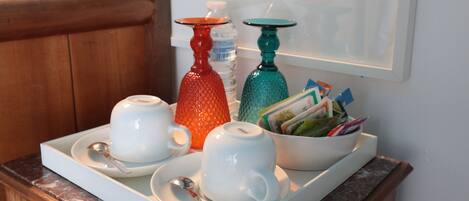 A wooden dresser with a tray holding white teacups, a red vase, and a teal vase with cards.