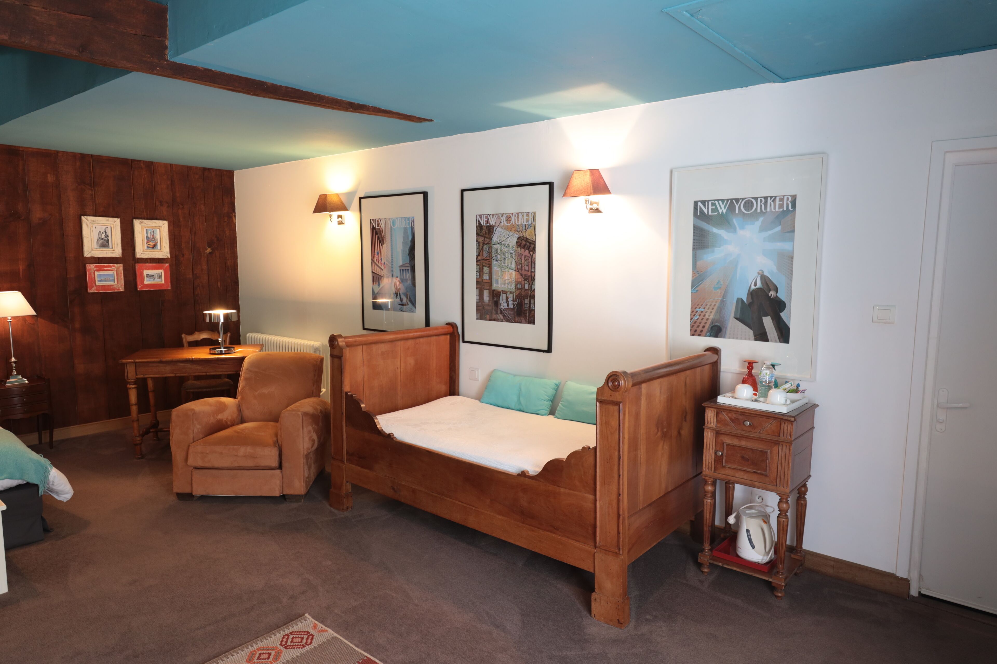 A bedroom with a wooden bed, a wooden chair, a small table, and a nightstand with a kettle.