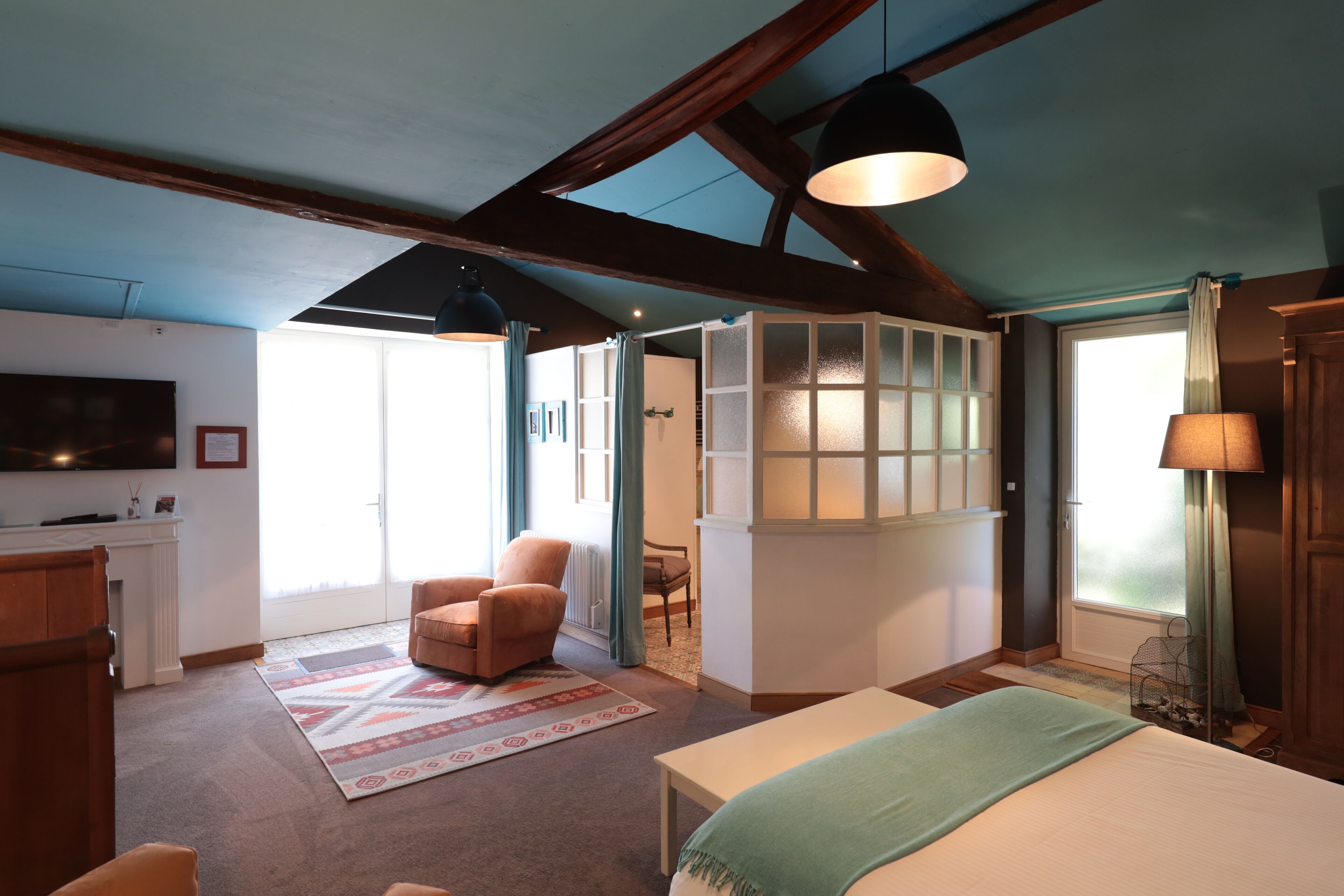 A spacious room with a large bed, a chair, a table, and a TV mounted on the wall.