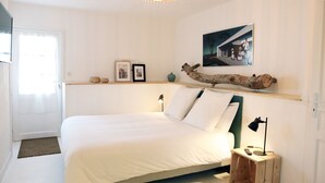 Une chambre avec un grand lit, une table de chevet avec une lampe, une étagère murale agrémentée d’objets décoratifs et une porte donnant sur l’extérieur.