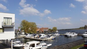 Un port de plaisance avec plusieurs bateaux amarrés, un bâtiment doté d’un balcon et une rivière en arrière-plan.