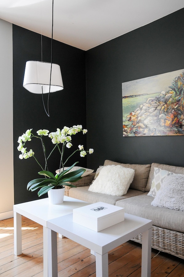 Un salon moderne avec un mur de couleur sombre, un canapé blanc, une table basse blanche, une orchidée en pot et un tableau.