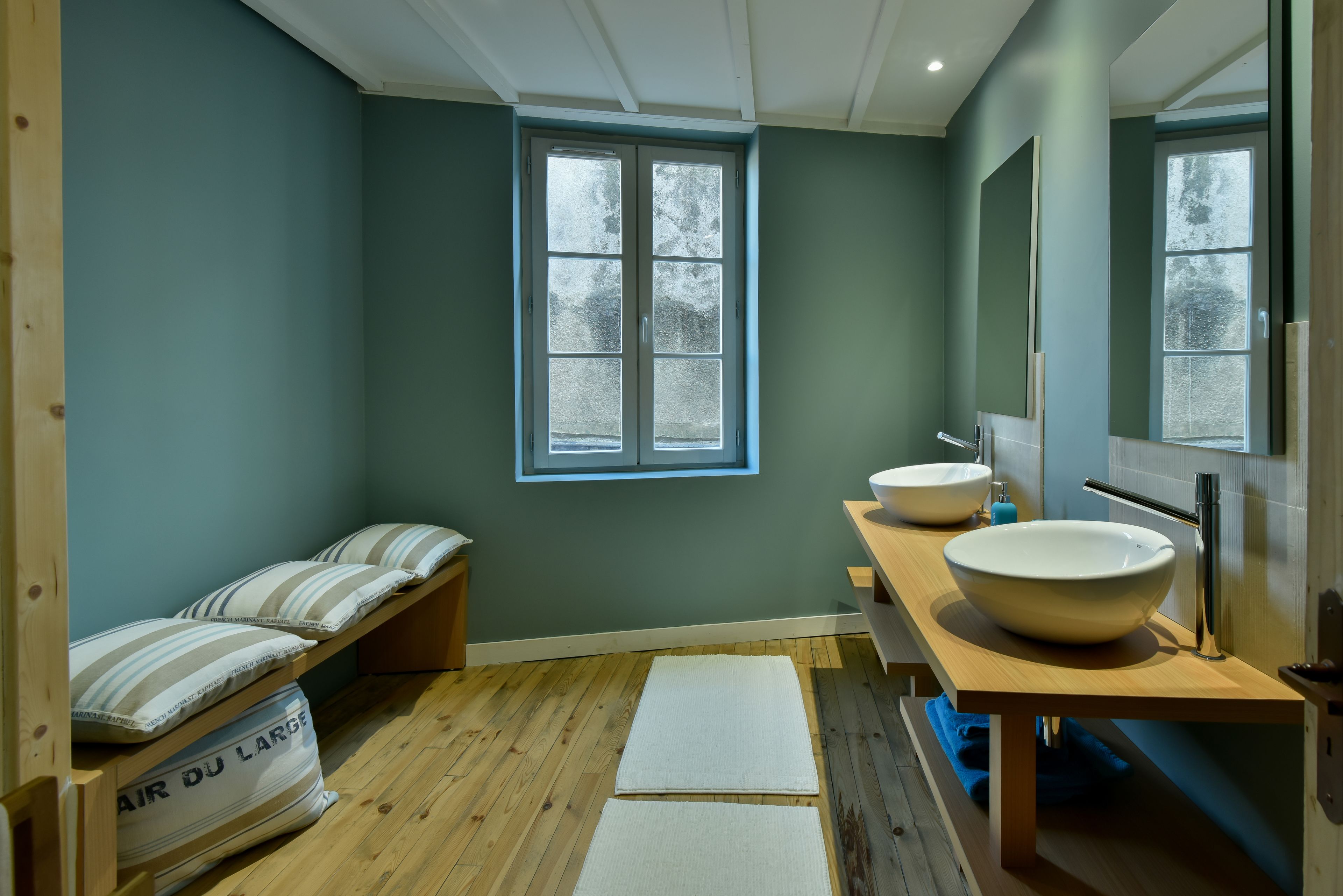 A bathroom with a large window, two sinks, and a wooden bench with pillows.