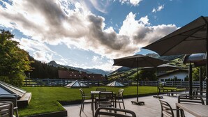 Un patio al aire libre con mesas y sillas, sombrillas y vistas a montañas y un pueblo.