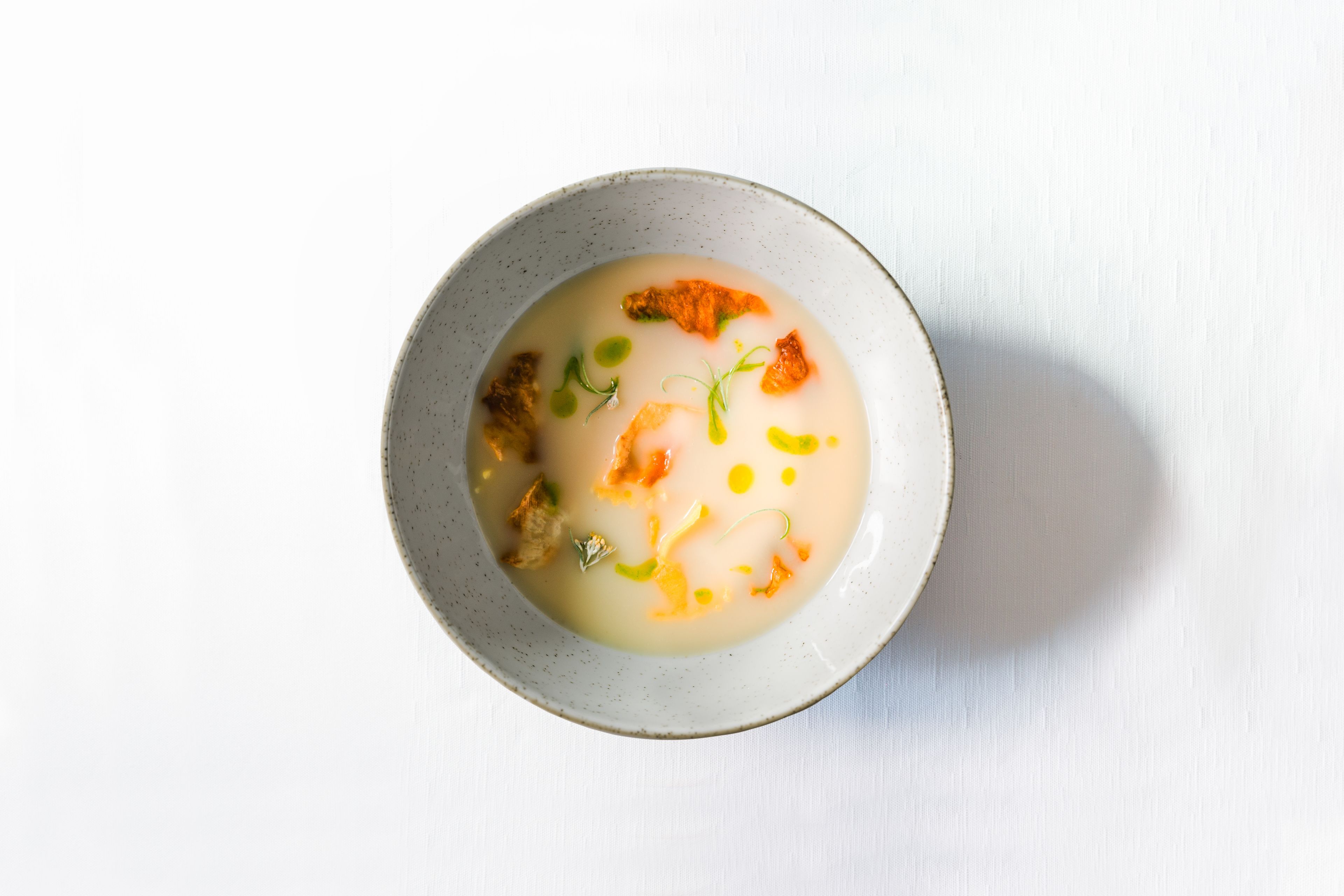 A bowl of soup with various ingredients, placed on a white surface.