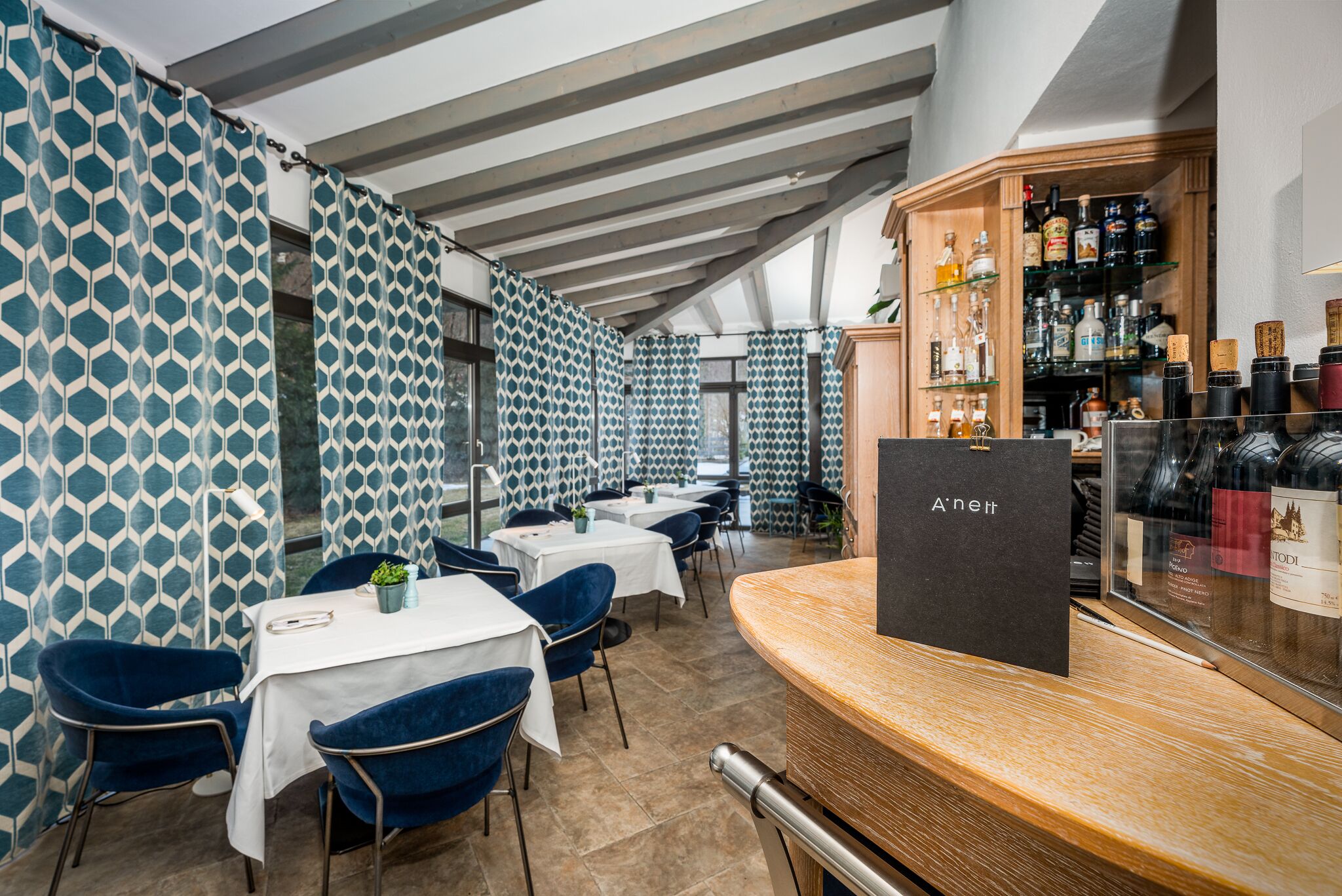 A restaurant with a modern interior, featuring patterned walls, blue chairs, and a bar area with a wine display.
