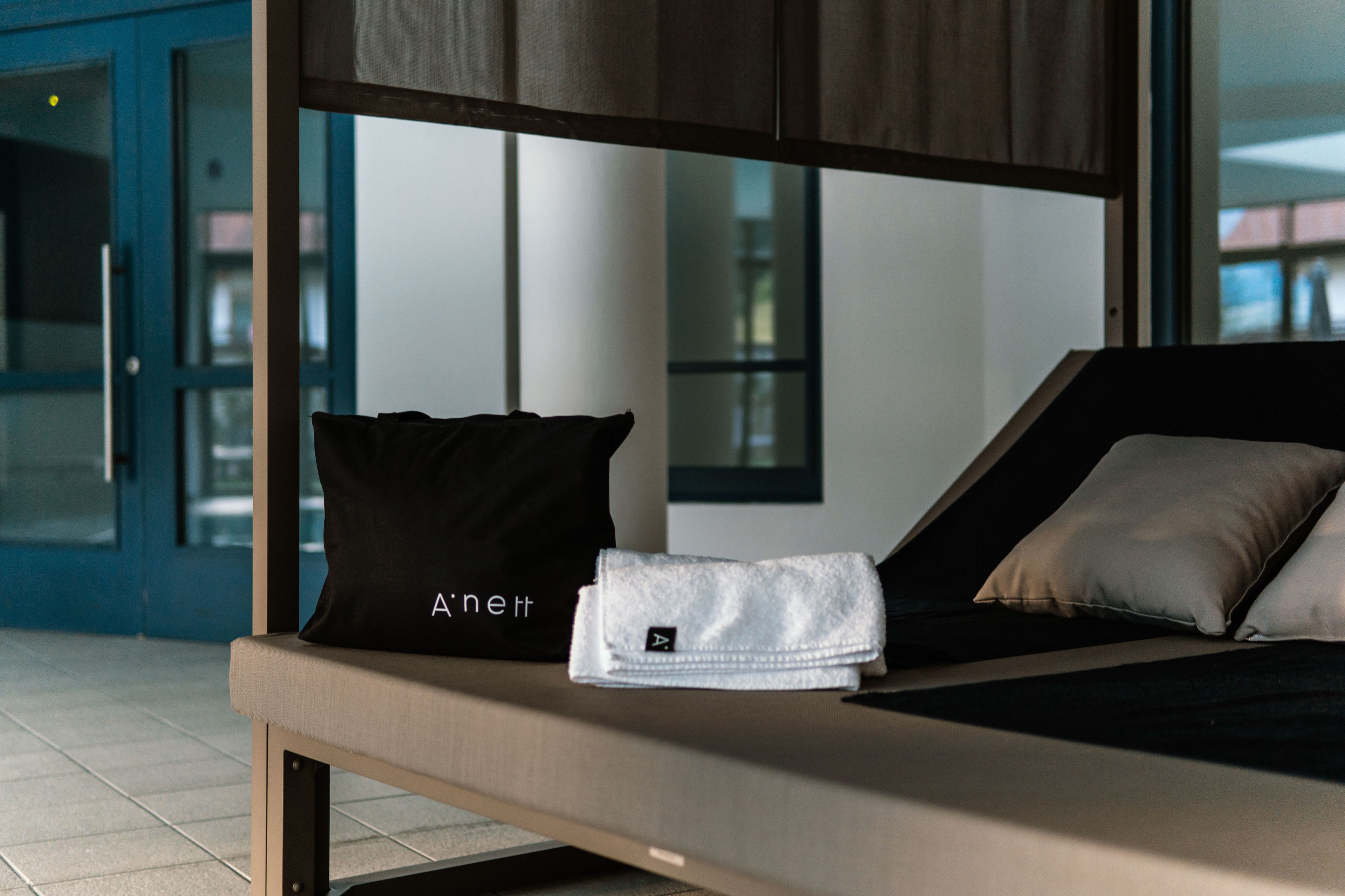 Een moderne hotelkamer met een bed, een zwart kussen, een witte handdoek en een kleine witte tas op het bed.