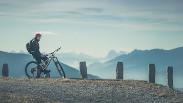 Una persona en bicicleta de montaña sobre un sendero de grava con pilares de piedra, rodeada de montañas.