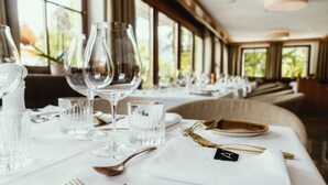 Una mesa de comedor dispuesta con copas de vino, vasos de agua y cubiertos, con un número en la servilleta.