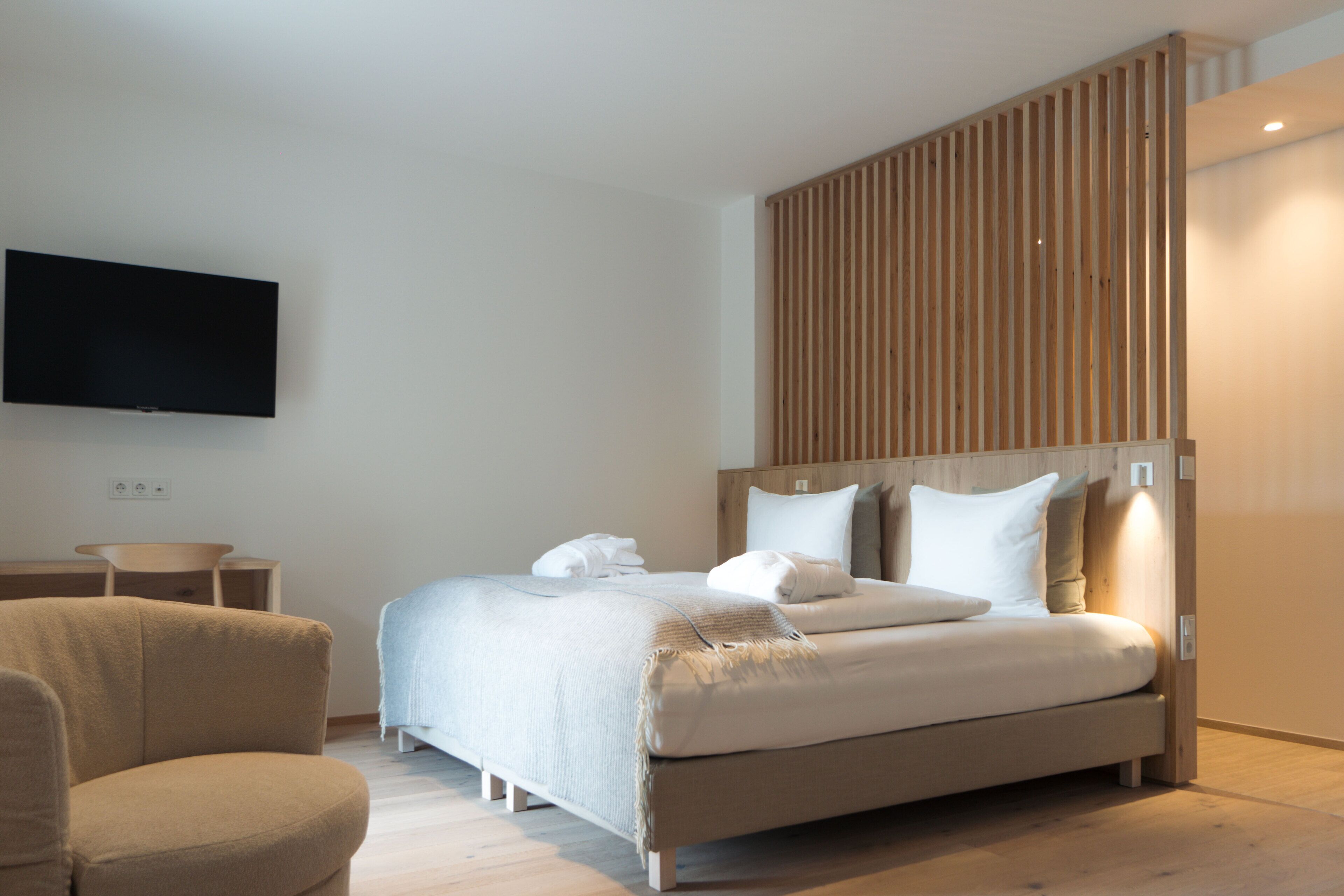 A modern bedroom with a bed, a TV mounted on the wall, and a wooden panel wall.