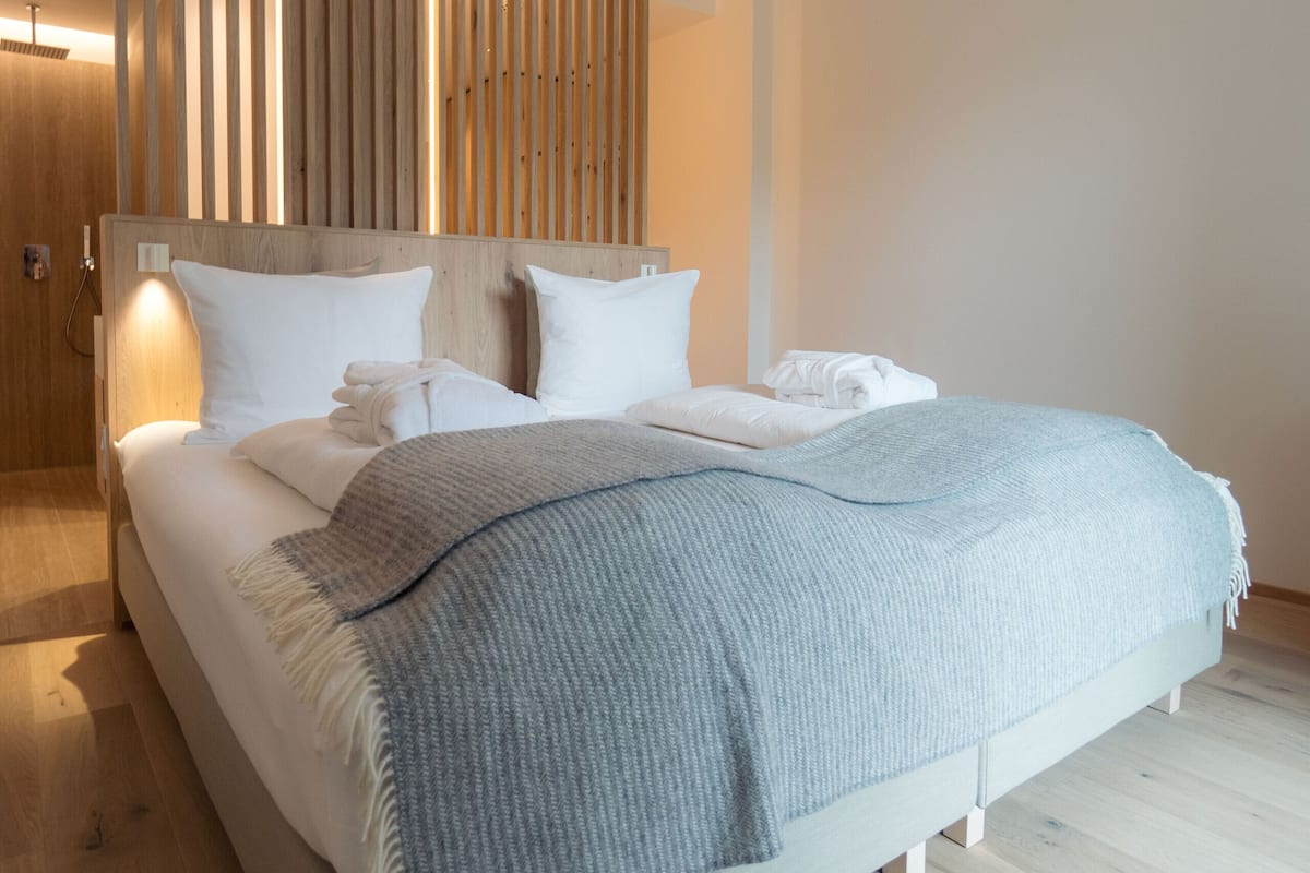 A modern bedroom with a wooden headboard, a large bed with white linens, and a grey throw blanket.