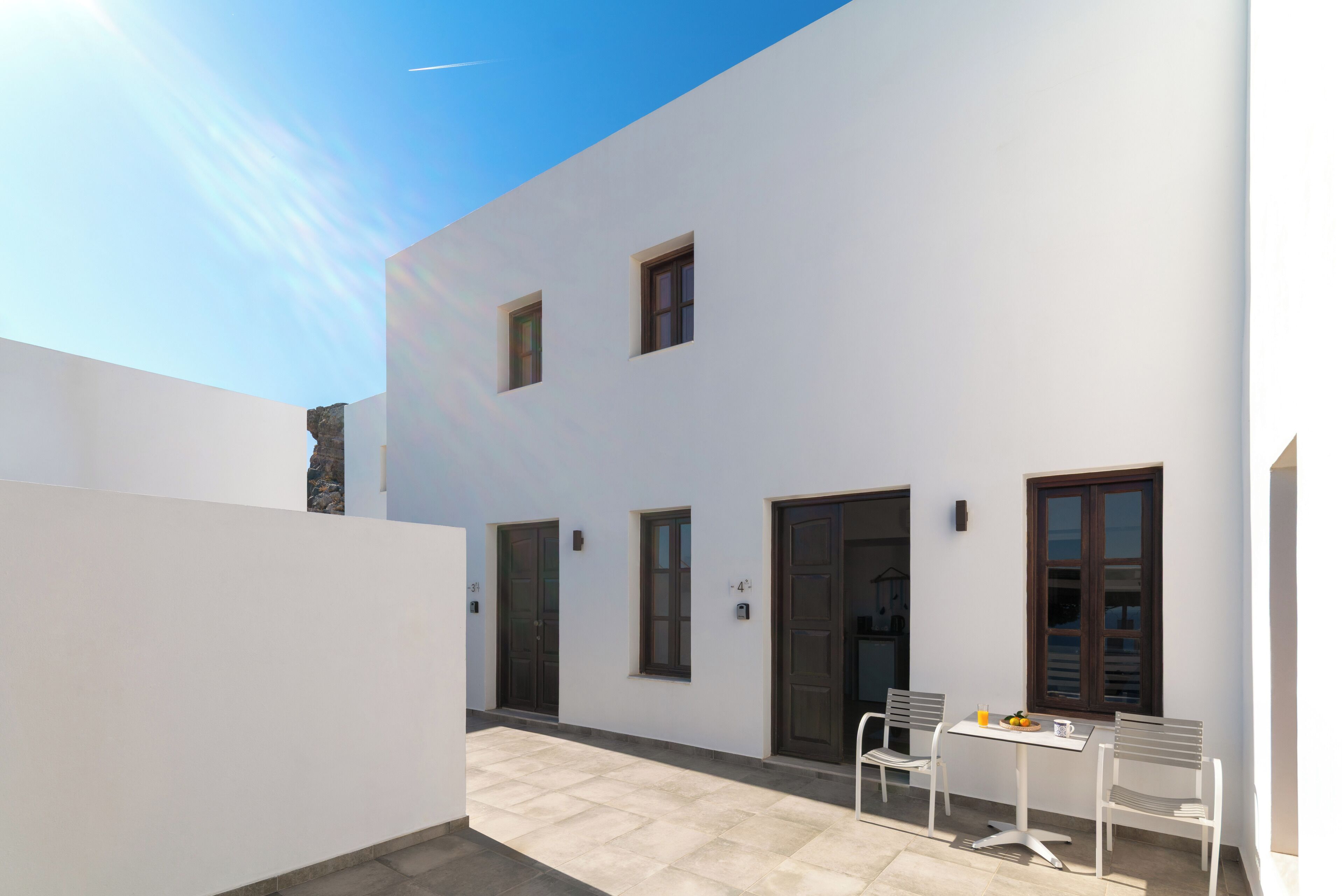 A modern building with a flat roof, white exterior walls, and a small patio area with a table and chairs.