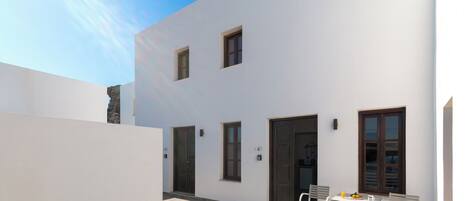 A modern building with a flat roof, white exterior walls, and a small patio area with a table and chairs.