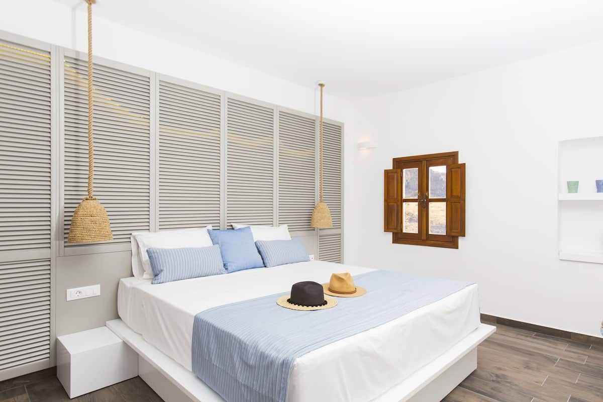 Une chambre moderne avec un grand lit, une fenêtre avec des volets en bois et un luminaire suspendu.