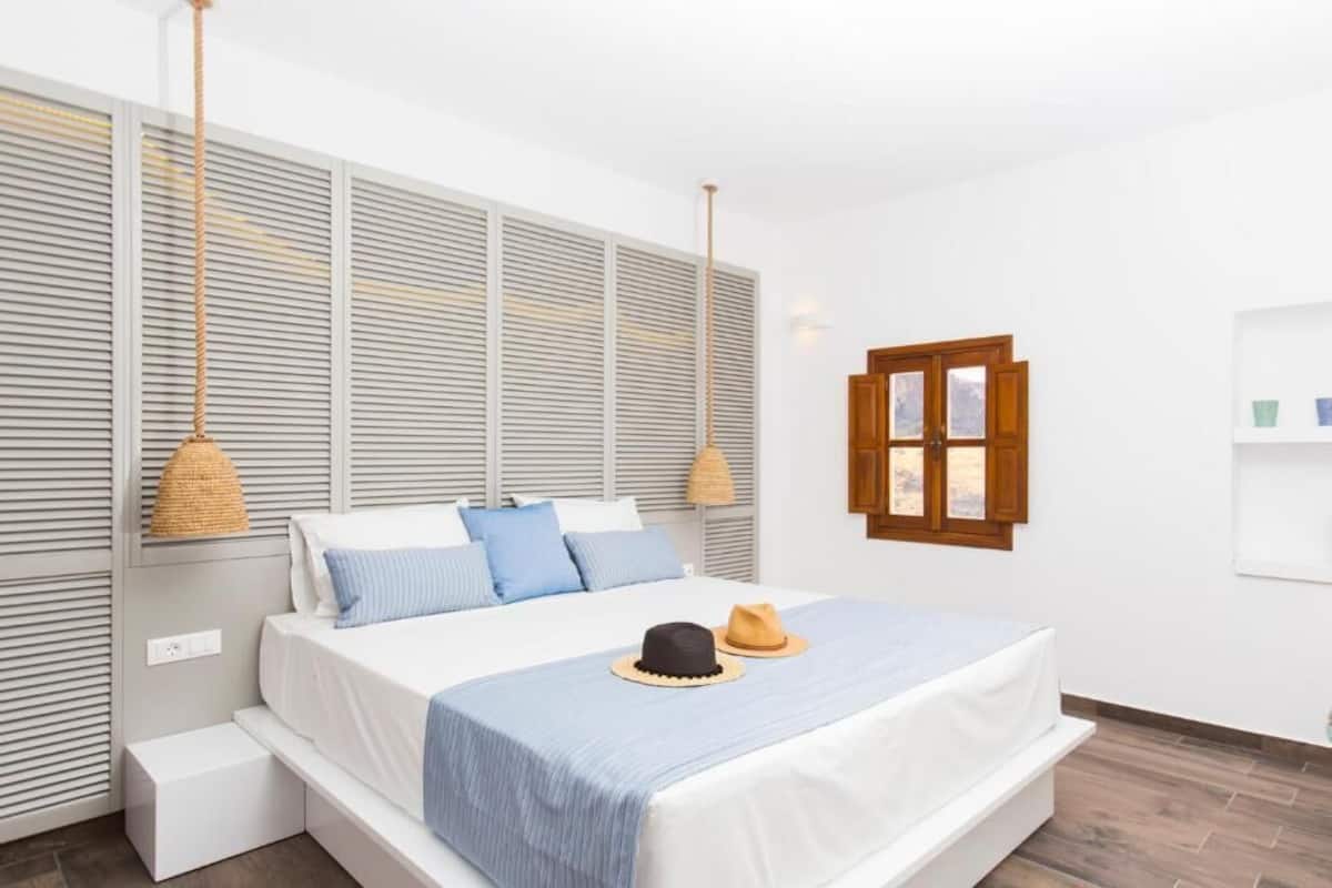 Une chambre à coucher comprenant un lit, des tables de chevet, une fenêtre et une étagère fixée au mur.