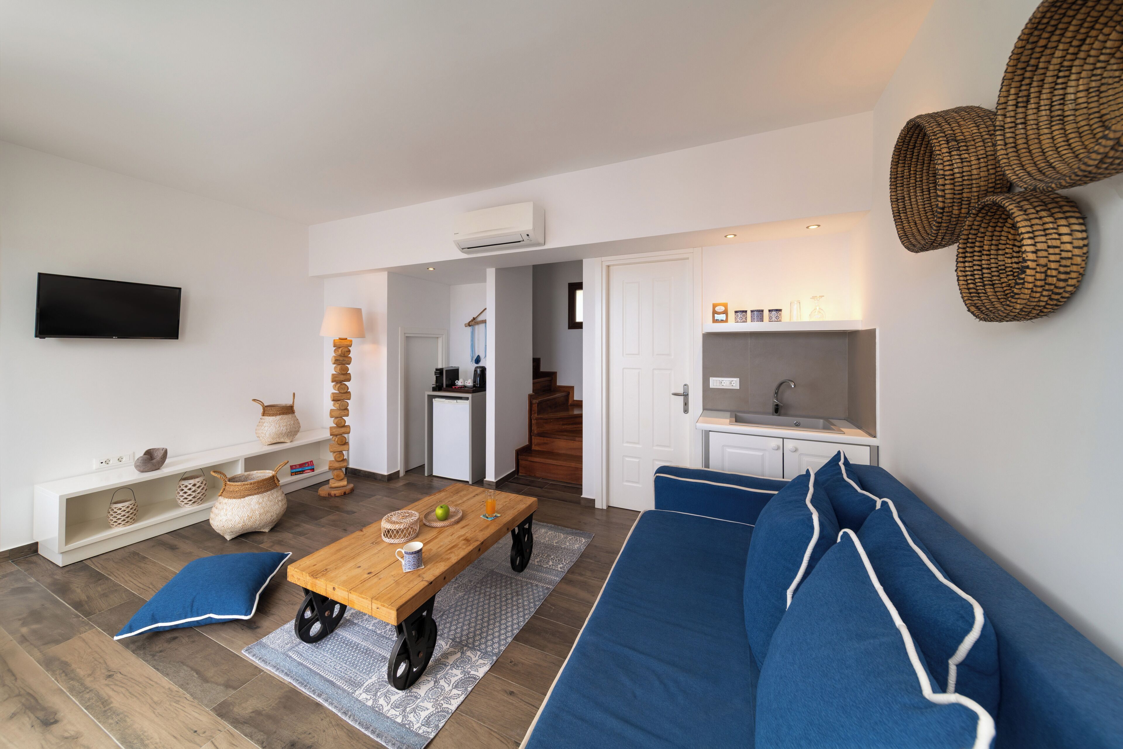 A modern living room with a sofa, coffee table, and a TV. There is a kitchen area with a sink and a staircase leading to another room.