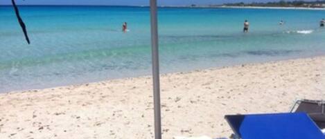 Una playa con una sombrilla azul, una silla de playa y una orilla arenosa.