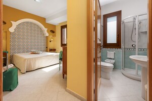 Une chambre d’hôtel avec un lit, une valise, une salle de bain avec douche et des toilettes.