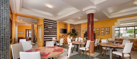 A restaurant with multiple dining tables and chairs, a wine rack, and framed pictures on the walls.