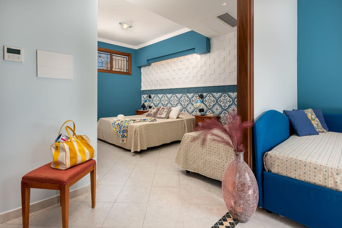 Una habitación con dos camas, una mesita con un bolso y un jarrón decorativo.