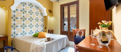 Habitación de hotel con cama, un escritorio con un florero, una maleta y un televisor en la pared.