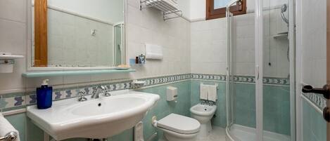 A bathroom with a sink, toilet, bidet, and a glass-enclosed shower.