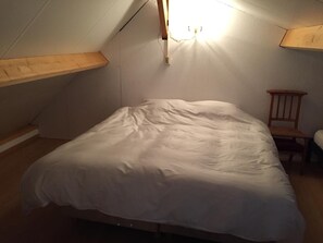 A small, dimly lit attic bedroom with a single bed, wooden headboard, and a chair. - B&B Logeren bij van Heeren (Made)