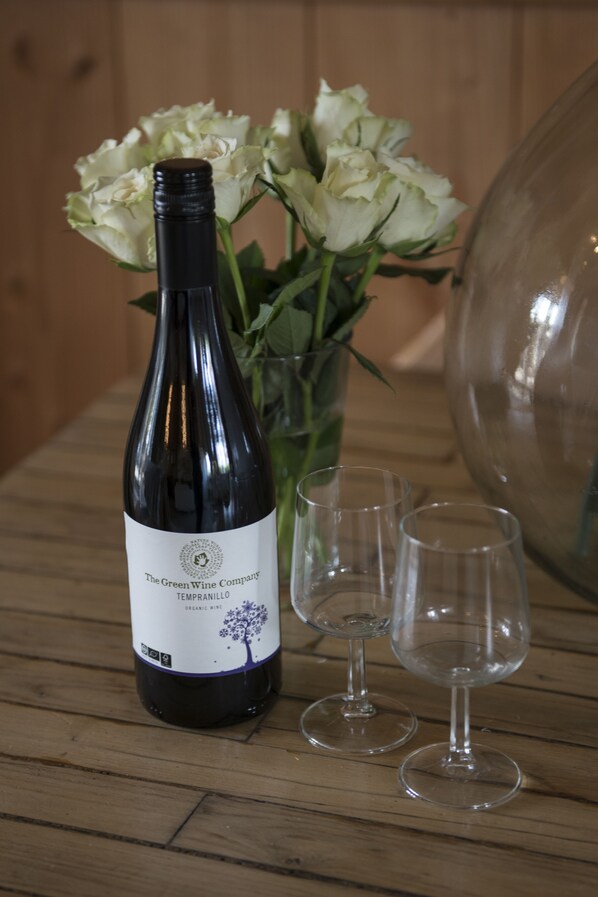 A wine bottle, two wine glasses, and a vase of white flowers on a wooden table.