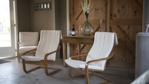 Two white cushioned chairs with wooden frames and a wooden table with a vase of flowers and a bottle of wine. - B&B Logeren bij van Heeren (Made)