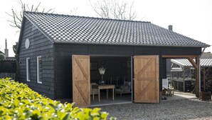A wooden building with a sloped roof and open wooden doors leading to an interior space with a table and chairs. - B&B Logeren bij van Heeren (Made)