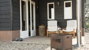 A wooden building with a porch, two chairs, a fire extinguisher, and a wicker basket. - B&B Logeren bij van Heeren (Made)