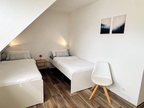 A small, triangular attic bedroom with two beds, a nightstand, a chair, and two wall-mounted pictures. - Ferienwohnung Weiher nähe Nürnberg Messe (Schwanstetten)