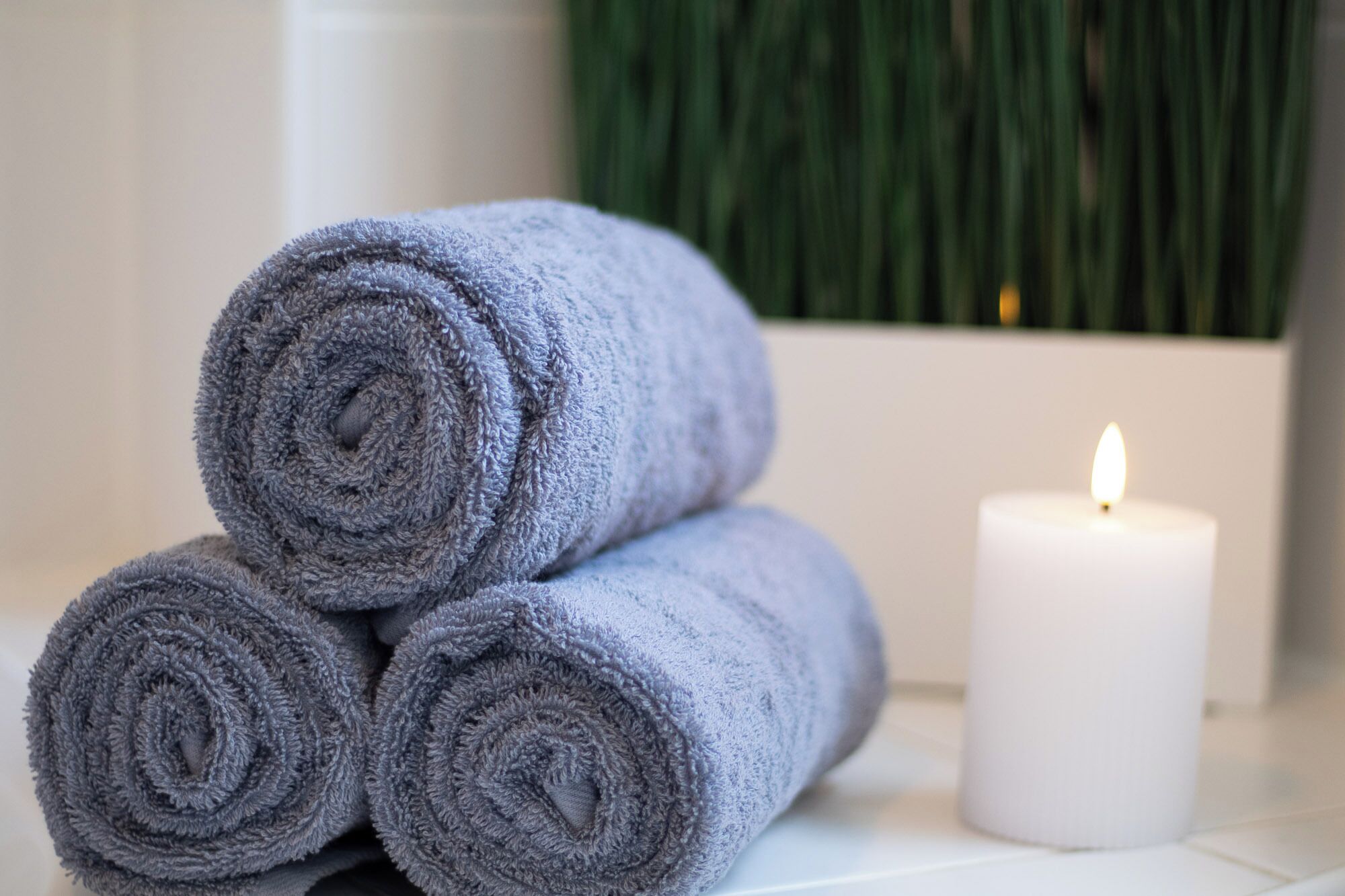 Three rolled towels and a lit candle on a white surface.