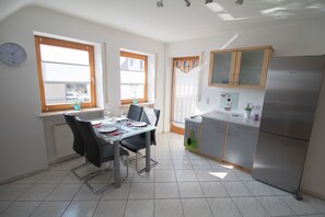 Une cuisine moderne avec un réfrigérateur en acier inoxydable, une table à manger avec des chaises et une fenêtre agrémentée d’une plante en pot.