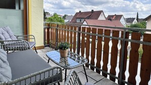 Ein Balkon mit Tisch und Stühlen, einem Blumentopf und Blick auf Häuser im Hintergrund.